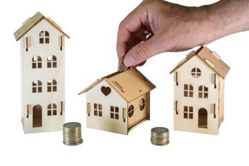 Hand placing coin into small wooden house piggy bank on transparent background, symbolizing saving for homeownership, real estate investment, mortgage planning and financial security