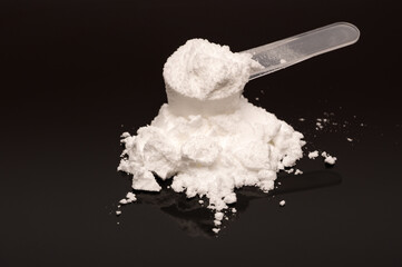 A scoop of creatine monohydrate powder on a black reflecting surface. Used by fitness enthusiast and recreational bodybuilding. 