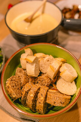 Table with cheese fondue dinner with bread and different vegetables. Traditional Swiss food at a ski holiday in the mountains like the Alps.