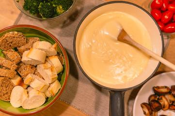Table with cheese fondue dinner with bread and different vegetables. Traditional Swiss food at a ski holiday in the mountains like the Alps.