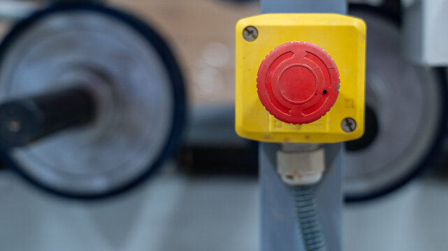 Emergency stop button on industrial machine with blurred rollers in background
