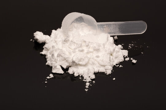 A scoop of creatine monohydrate powder on a black reflecting surface. Used by fitness enthusiast and recreational bodybuilding. 