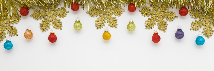 Beautiful shiny golden tinsel, snowflakes and colorful baubles on light gray table background. Closeup. Christmas decoration. Wide banner. Empty place for text. Top down view.