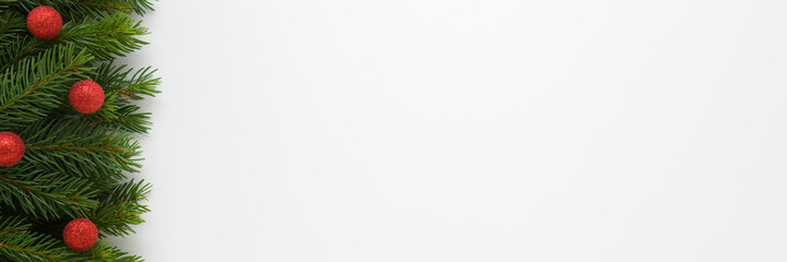 Red baubles with glitter and green natural fresh fir branches on light gray table background. Closeup. Christmas decoration. Wide banner. Empty place for text. Top down view.