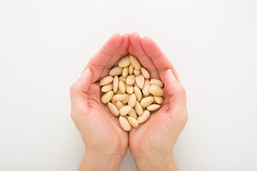 Young adult woman opened palms holding heap of almond nuts on light gray table background. Closeup. Point of view shot. Top down view.