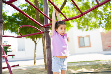 Girl experiencing childhood fun by hanging on monkey bars at a park, developing physical strength and motor skills