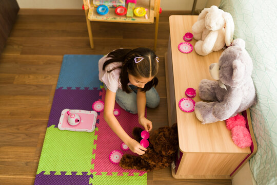 Top view of little girl playing make-believe tea party with toy animals, developing imagination and social skills at home
