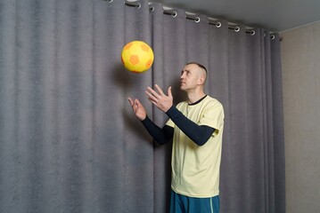 A man is tossing a soccer ball up in the air. Warming up with the ball before a fitness session. Home fitness workout. Playing sports with a ball at home.