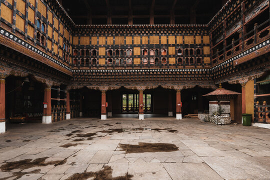 View of a courtyard featuring detailed woodwork and architecture with a wet stone floor reflecting ambient light in Rinpung Dzong, Paro, Bhutan.