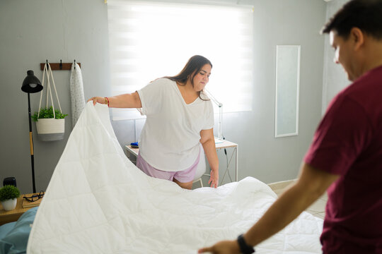 Adult couple making their bed in a modern bedroom, collaborating on household chores and daily routine - Powered by Adobe
