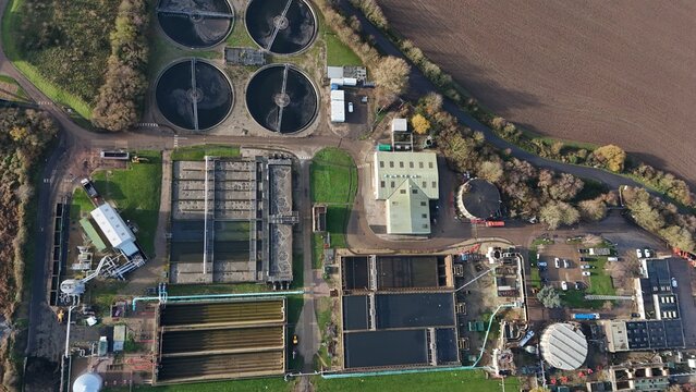 Aerial view of a complex industrial site with circular tanks and rectangular structures, showcasing a blend of grey concrete and green vegetation, Kings Lynn, United Kingdom.