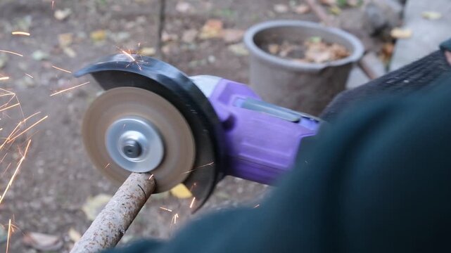 Top view over the shoulder, a man gloved hand uses a cordless disc cutting machine to cut a part from a horizontal metal pipe, cordless power tool, purple color