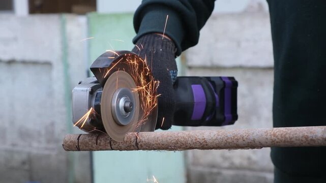 Close-up of a man s hand in a black glove using a cordless cut-off machine to slice a thin metal tube. Sparks from the metal cutting fly and glow. Home maintenance work with a purple power tool.