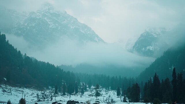 A snowy winter landscape in mountain valley with clouds floating around. Light snowfall during moody winter day in Aru valley, Kashmir, India. Winter wonderland of India. 