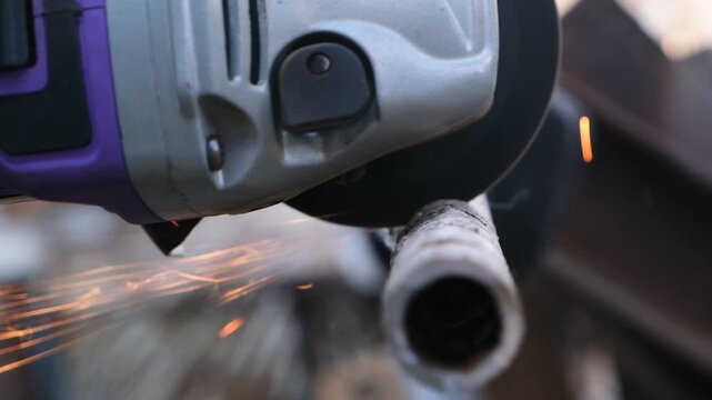 Cordless disc cutting machine cuts a metal pipe, producing orange sparks flying aside. Metal cutting, home and repair work, DIY, maintenance, handheld tool in action