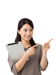 Smiling Asian woman enthusiastically points towards an empty space while holding a digital tablet, directing attention and showcasing a clear concept for business or lifestyle presentation
