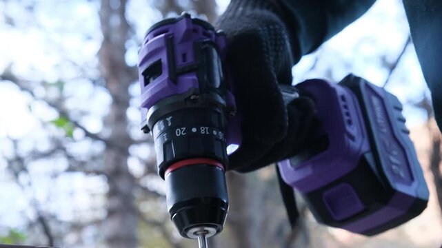 Low angle view of a mans hand firmly holding a cordless electric drill pressing on a wooden board for faster drilling top view purple cordless drill woodworking craftsmanship