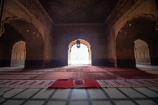View of warm sunlight filtering through the arched entrance of a mosque, illuminating the carpeted floor in Badshahi Masjid Mosque, Lahore, Pakistan.