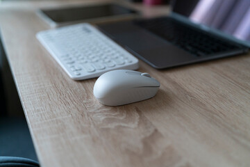 A computer mouse sits on wood near a keyboard and laptop during a work session