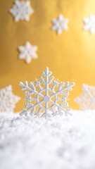 White snowflake decorations on a bed of artificial snow with a golden background, creating a festive winter scene.