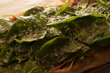 Closeup spinach pizza with cheese, baby spinach leaves, generous parmesan grate, golden crust edges, olive oil drizzle,
