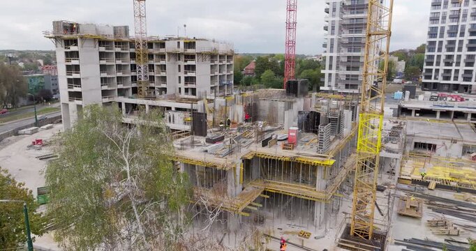 Aerial drone shot of high-rise residential blocks under construction in the heart of Katowice, Poland. Cranes, scaffolding, and concrete structures reflect dynamic urban growth.