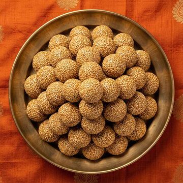 Top view tilgul ladoo arranged in a mountain like mound inside a polished brass plate on a clean festive background for premium makarsankranti food visuals