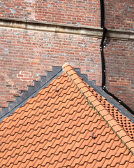 View of a terracotta roof with textured tiles against a brick wall in a historic neighborhood during daylight
