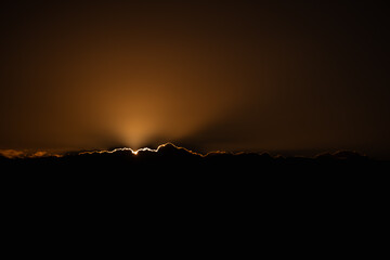 Sun rays emerging from behind the clouds during sunset in Tenerife. Dark horizon contrasted with glowing, golden sky.