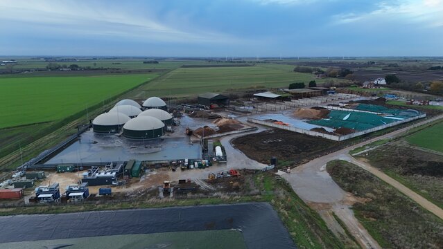 Aerial view of the biogas plant with its cluster of dome-shaped digesters casting shadows on the wet ground, contrasting against the surrounding green fields, Wisbech, England, United Kingdom.
