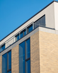 Modern building design featuring large windows and balcony under clear blue sky
