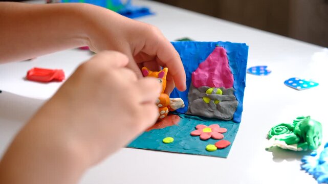 Child smearing colorful plasticine on cardboard and creating fairy tale card with cartoon animals, using nature details also, dry flowers, cone, leaves. Hobby. DIY