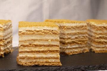 closeup layered honey cake slices showcasing creamy filling, delicate golden crumbs and defined sponge layers on dark slate