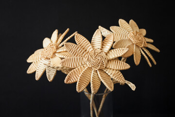 A bouquet of flowers made of straw in a glass vase on a black background. Straw weaving
