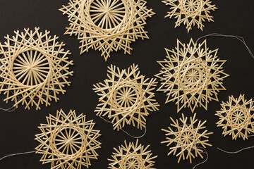 Snowflakes are made of straw on a black background. Straw snowflakes. Christmas decor. Top view. Straw weaving. Lutsk, Ukraine
