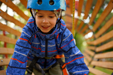 Close-up of an excited young boy concentrating while navigating a wooden obstacle tunnel on a thrilling high ropes course.