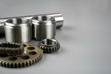 Close-up of metallic mechanical components, including gears, bushings, and a cylinder, resting on a clean light grey background with copy space.