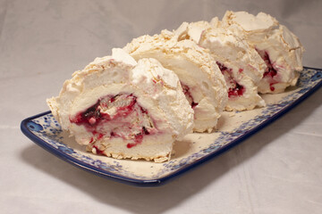 Raspberry meringue roll with cream swirl and airy texture, sliced roulade plated on decorative dish, light and delicate dessert