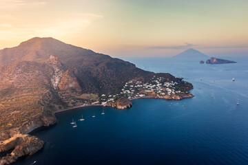 Aerial view of a rugged coastline meeting the tranquil sea, with a small village nestled along the shore, Panarea, Sicily, Italy.