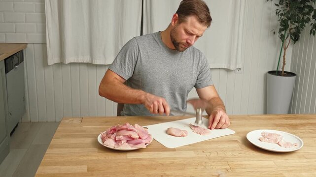 Person using meat tenderizer on raw chicken. Chef preparing pork loin slice with meat mallet on cutting board. Man tenderizing fillet. Cooking cutlets pounding poultry breast close-up. Culinary dish.