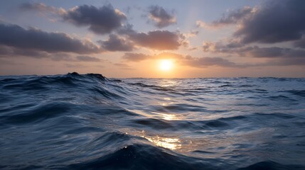 A dramatic sunset with warm hues paints the sky over dark blue undulating ocean waves creating a serene and atmospheric seascape