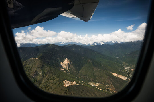 Aerial view of lush green mountains meeting a blue sky dotted with fluffy white clouds from the window of a plane, Flight from Bumthang to Paro, Bhutan.