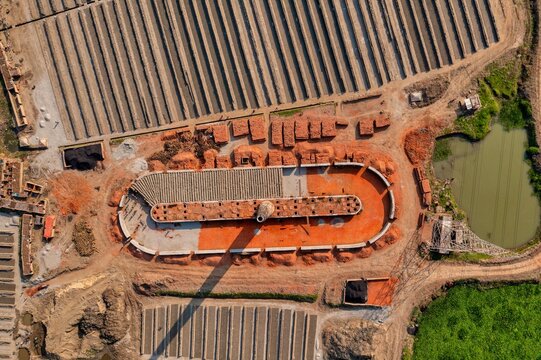 Aerial view of vast brickyards with patterns of drying bricks alongside a circular structure, casting shadows in the landscape, Aminbazar, Dhaka Division, Bangladesh.