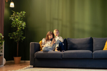 Brother and sister watching something on smartphone sitting on sofa at home
