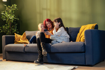 Mother showing smartphone to children while relaxing on sofa at home