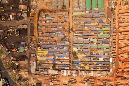 Aerial view of tightly packed, colorful buildings contrasting with the muddy earth and dark piles, creating a vibrant tapestry from above, Aminbazar, Dhaka Division, Bangladesh.