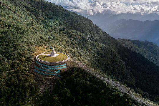 Aerial view of a serene temple complex atop a verdant mountain, with the sky's gentle light casting shadows on the undulating landscape, Chele La Pass Laptsa, Paro, Bhutan.