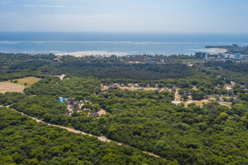 Aerial view of lush green canopy meets the azure ocean, fringed by sandy beaches and buildings, a vibrant coastal panorama., Bamburi, Mombasa, Kenya.