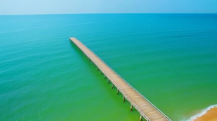 Long wooden pier extending into vast turquoise ocean water under clear sky