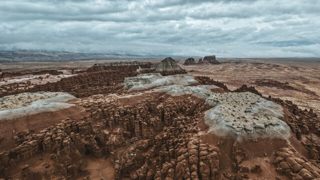 Aerial view of the otherworldly Goblin Valley unfolds in muted browns and grays beneath a brooding sky, a desolate landscape sculpted by time, Green River, Utah, United States.